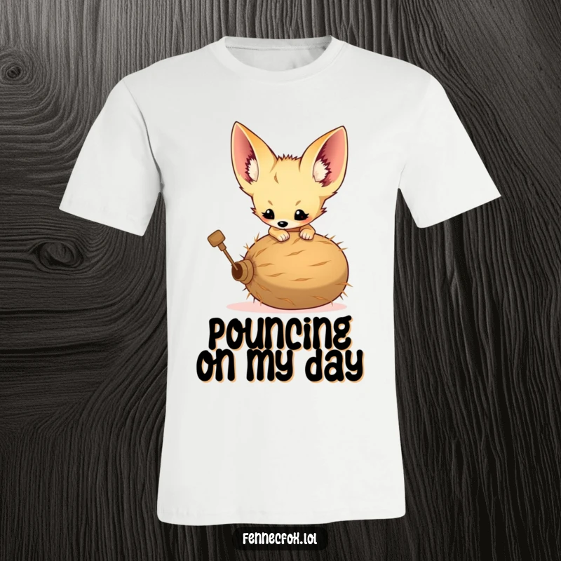 Funny t-shirt of a fennec fox kit with comically large ears leaping at a rolling tumbleweed with playful energy.